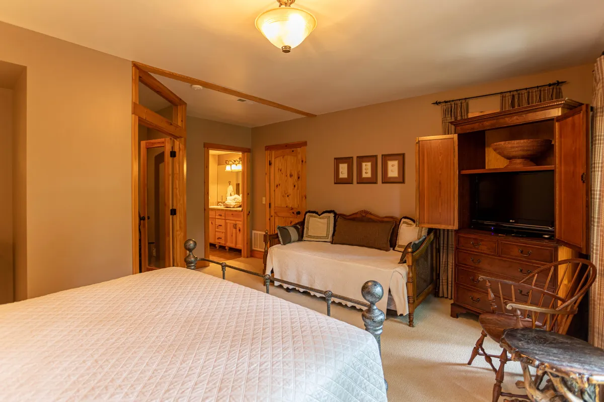 A spacious bedroom showcasing two separate beds (likely a queen and a twin), wooden furniture, decorative wall art, and a television. The environment is relaxed and inviting—ideal for families or small groups.