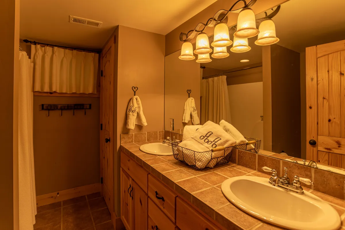 A bright, elegant bathroom with a double sink vanity, decorative light fixtures, and neatly arranged monogrammed towels. The atmosphere is spa-like and soothing—perfect for morning routines or winding down at night.
