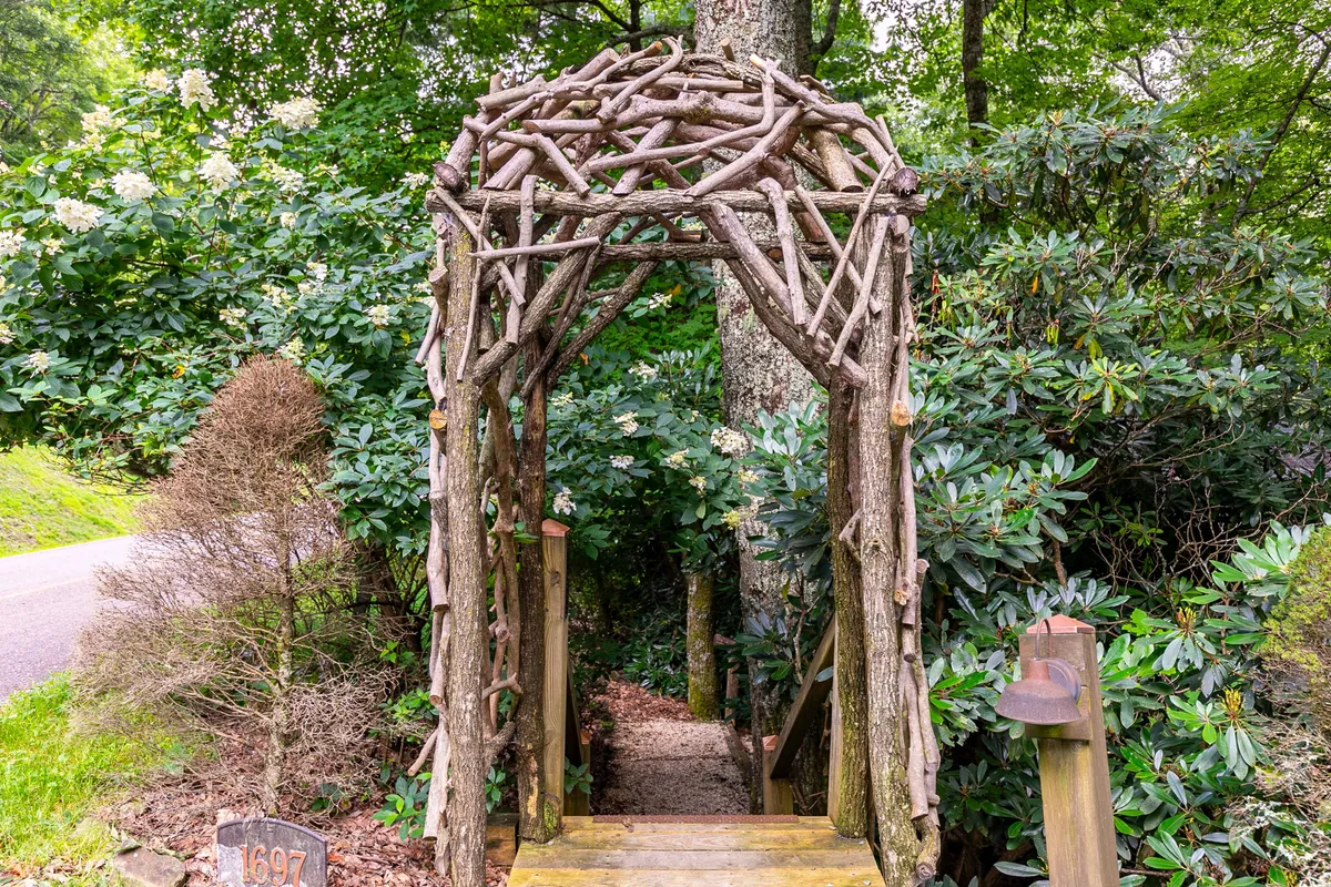 A whimsical exterior garden scene featuring a wooden archway surrounded by lush greenery. A winding pathway leads forward, inviting guests to stroll and discover hidden nooks, capturing the peaceful ambiance of the outdoors.