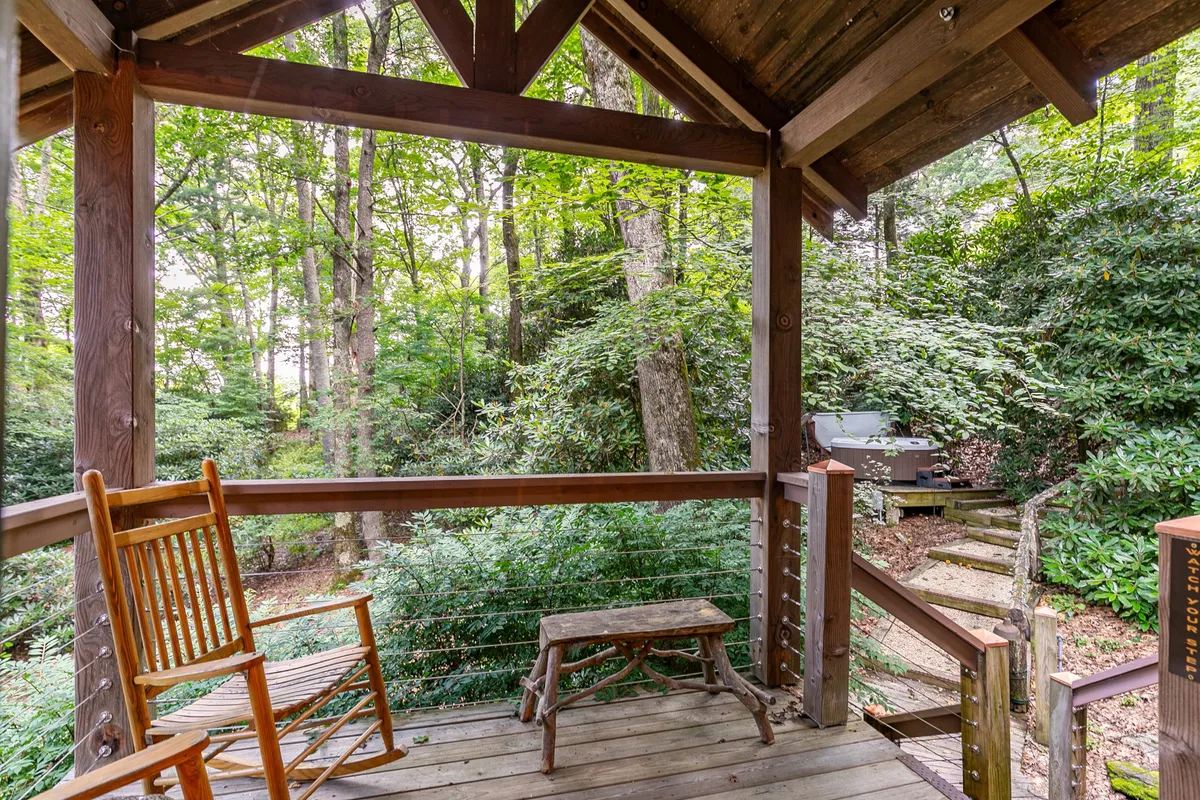 A cozy porch scene featuring a classic wooden rocking chair and stool, with greenery framing the background. The inviting setup encourages peaceful moments—reading, relaxing, or enjoying conversations as the sun sets or stars emerge.
