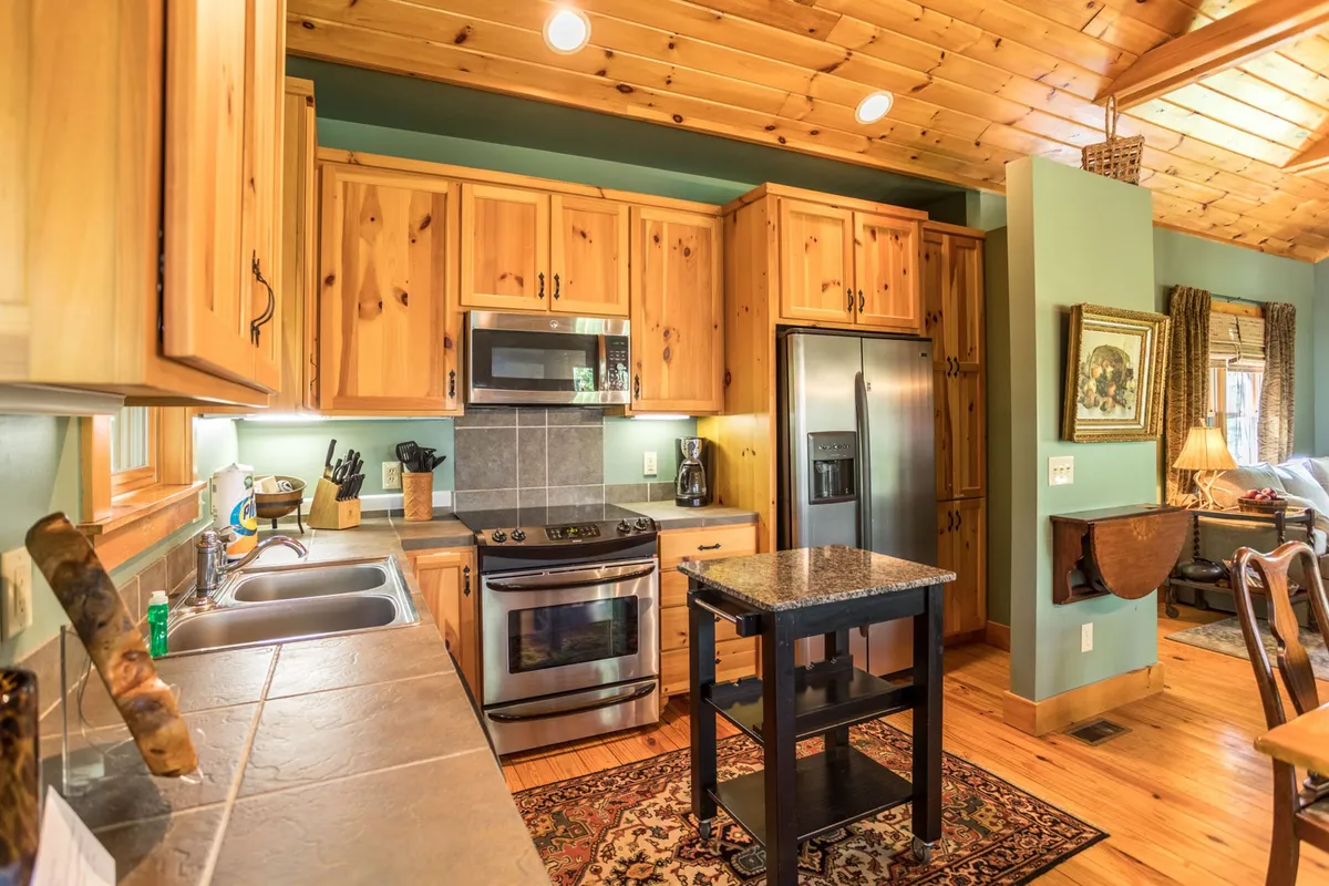 This image showcases the fully equipped kitchen, featuring stainless steel appliances, wooden cabinets, a kitchen island, and a decorative rug. The space is well-lit and inviting, ideal for preparing and sharing home-cooked meals.