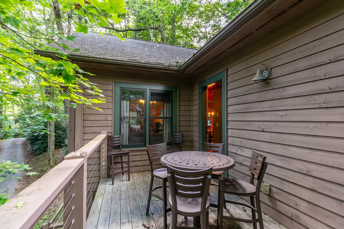 A spacious wooden deck featuring an outdoor table set for dining, surrounded by lush greenery. The scene is inviting, with the table positioned perfectly for enjoying morning coffee or sunset meals in the fresh mountain air. The deck's open design maximizes the connection to nature and provides ample space for social gatherings or quiet relaxation.
