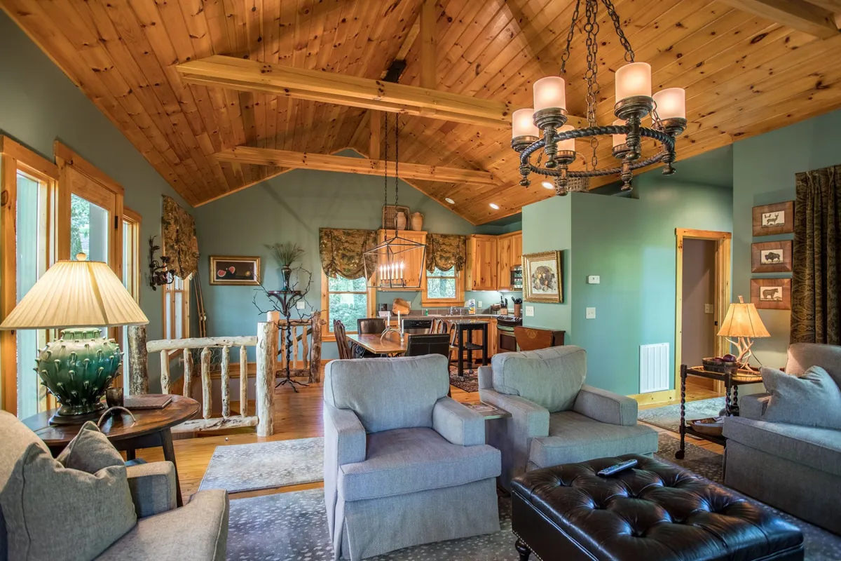 A welcoming open-plan interior showcasing comfortable seating, rustic wooden beams, a glowing chandelier, and a cozy kitchen area. The space is arranged for family gatherings, casual dining, and moments of relaxation, all in one inviting setting.