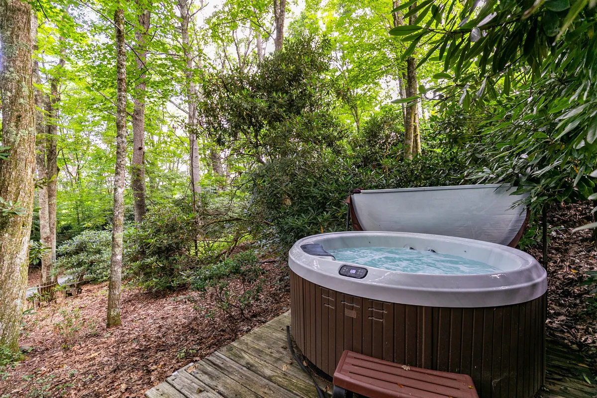 A serene outdoor setting featuring a hot tub nestled on a wooden deck surrounded by trees. The view emphasizes immersion in nature, perfect for relaxing soaks in a tranquil environment.