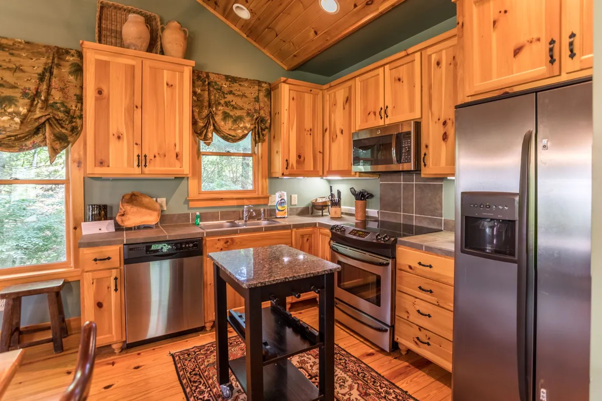 A bright, well-equipped kitchen with wooden cabinetry, granite countertops, large windows offering natural views, and modern appliances. The space feels cozy and functional, perfect for preparing quick meals after a day outdoors or enjoying family gatherings.